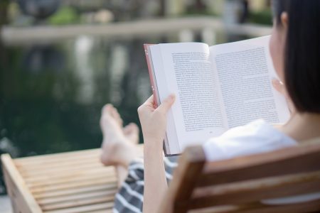 woman reading book in deck chair near swimming pool